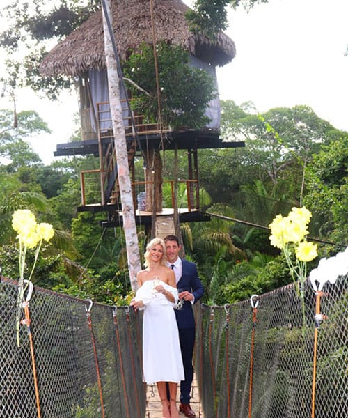 A bride and groom standing on a tree house bridge, surrounded by lush greenery and a serene atmosphere.